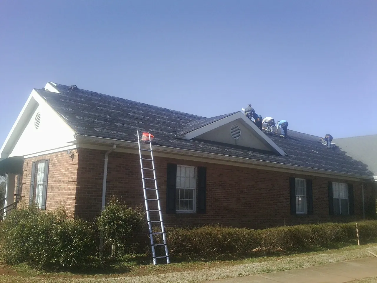 Crew tearing shingles off a brick ranch roof with a ladder set — Emergency Roof Repair work by our crew in Le Grand
