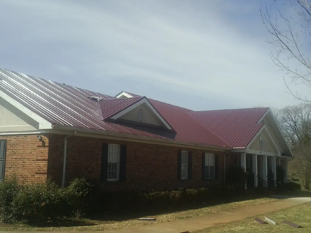 Red metal roof with gabled entries on a long brick building, from a Hail Damage Roof Repair job in Le Grand