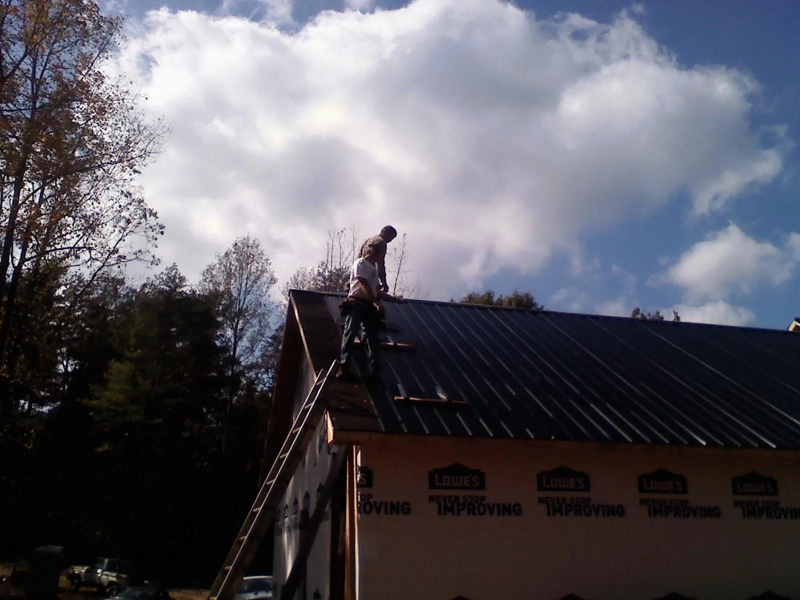 Roofer fastening dark metal panels high against a cloudy sky, from a Roof Inspection job in Le Grand