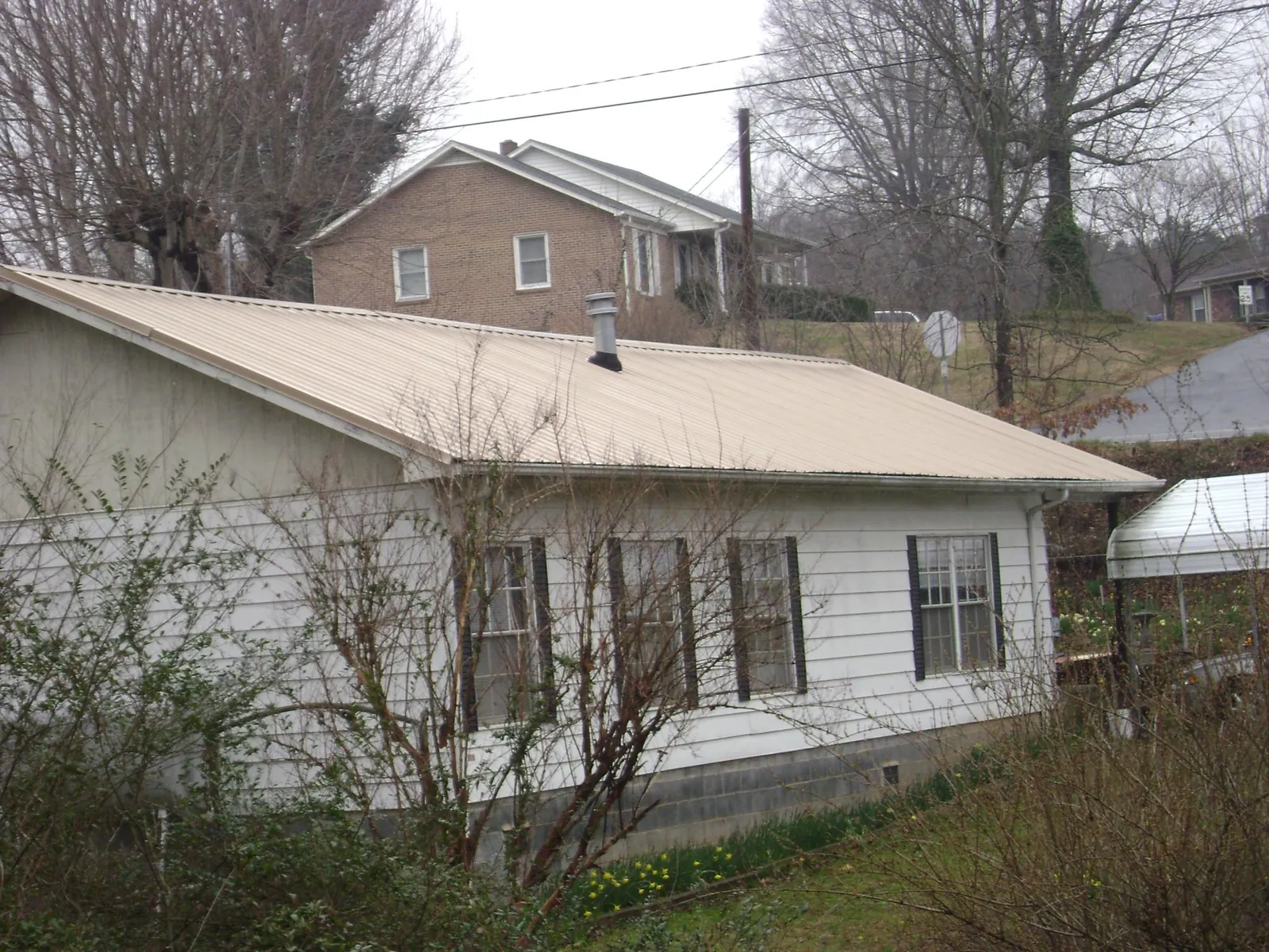 Tan metal roof on a white sided house set into a hillside — Commercial Roofing by Roofing Brothers in Le Grand